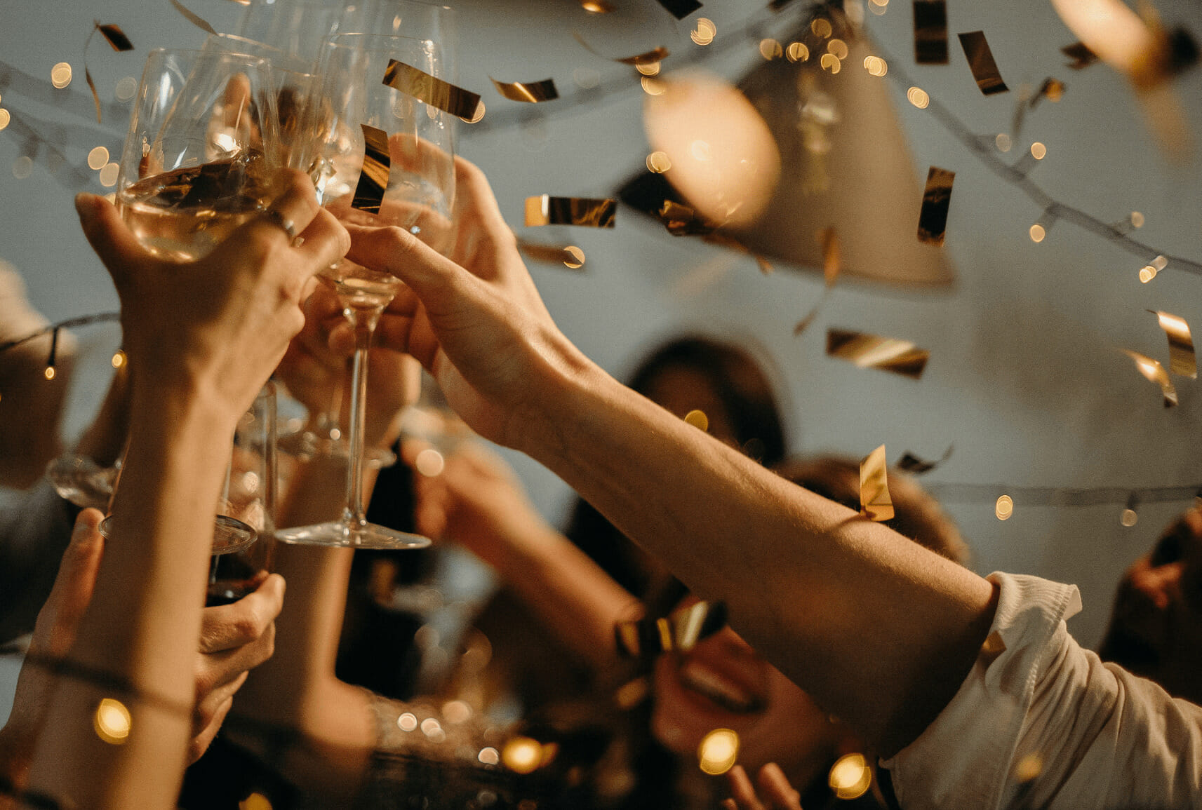 街コンで乾杯する様子。飛び散る金色の紙吹雪の中、複数の手がワイングラスを掲げ合っている。セレブレーションの雰囲気が感じられる華やかな一コマ。